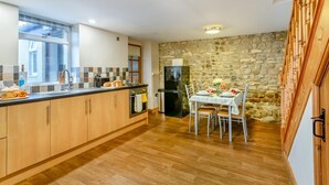 A modern kitchen with wooden cabinets, a stone wall, and a dining area with a table set for four. - 2 Bed in Thornton Watlass (oc-m30203) (Thornton Watlass)