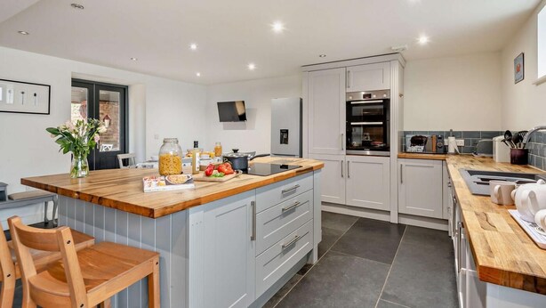 A modern kitchen with grey cabinets, a wooden island, and a built-in oven. - 3 Bed in Heacham (oc-t30182) (Heacham)