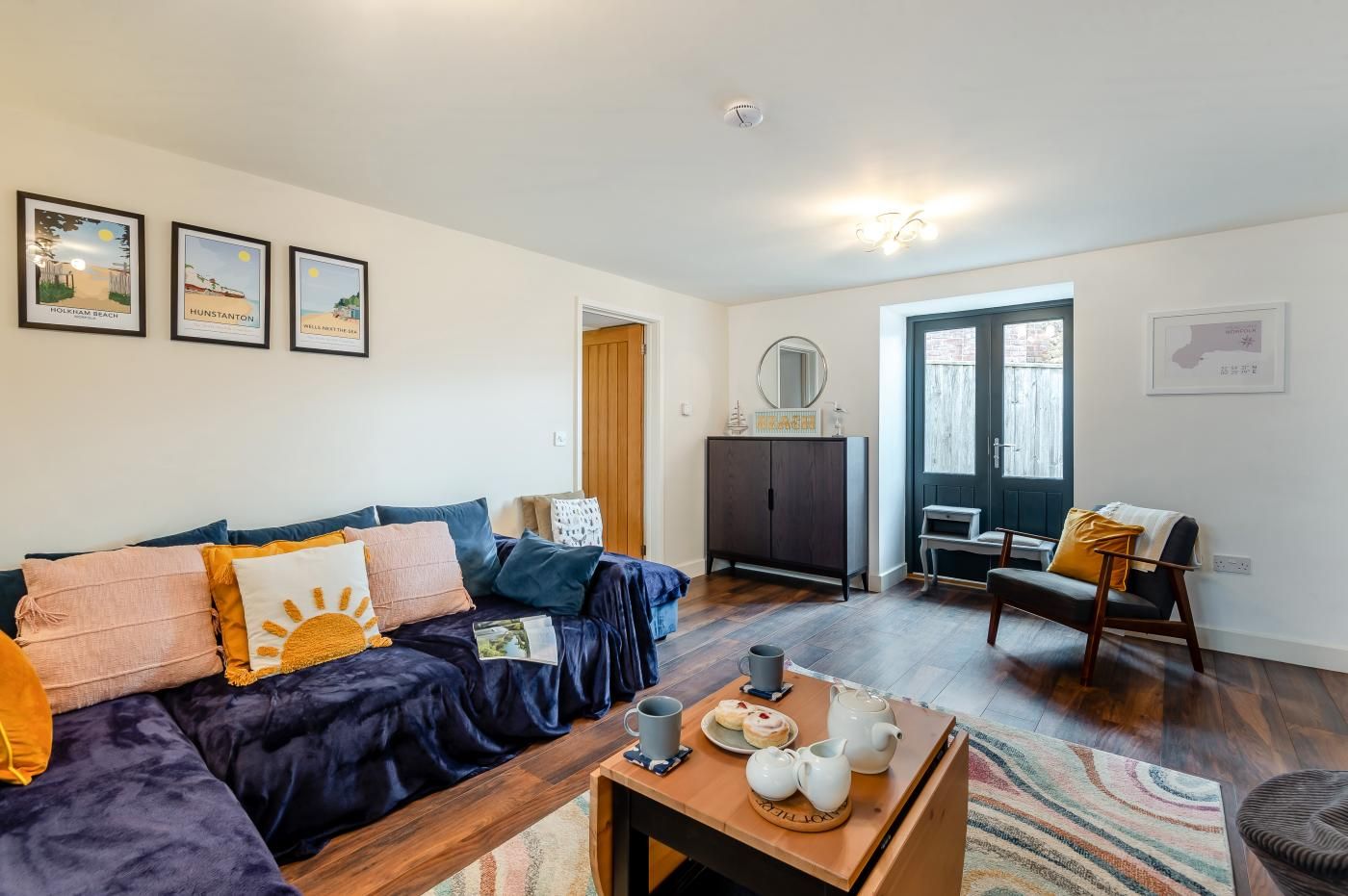 A living room with a dark blue sofa, a coffee table with a teapot and cups, and framed pictures on the wall.