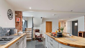 A modern kitchen with a central island, a dining area with a chair, and a staircase leading to another level. - 3 Bed in Heacham (oc-t30182) (Heacham)