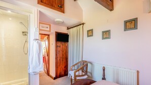 Een slaapkamer met een bed, een houten stoel, een douche en een deur naar een andere kamer.
