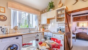 Een compacte keuken met een wasmachine, een eethoek met een glazen tafel, en een slaapkamer met een bed en nachtkastje.