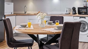 A modern kitchen with a dining table set for breakfast, including bowls, glasses, and a vase of flowers. - Apartment Lurdes (Arco da Calheta)