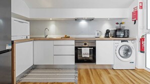 A modern kitchen with white cabinets, a stainless steel refrigerator, a built-in oven, a dishwasher, a microwave, and a washing machine. - Apartment Lurdes (Arco da Calheta)