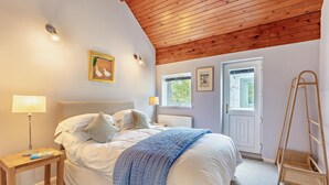 Un dormitorio con cama, lámparas de noche, una escalera de madera y dos ventanas.