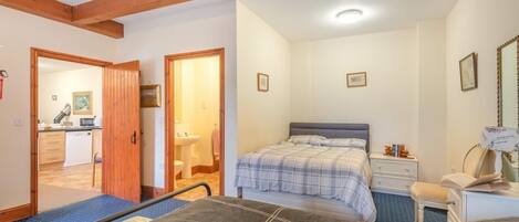 Un dormitorio con cama, mesita de noche y escritorio con silla. Se ve un baño con lavamanos e inodoro a través de una puerta abierta.