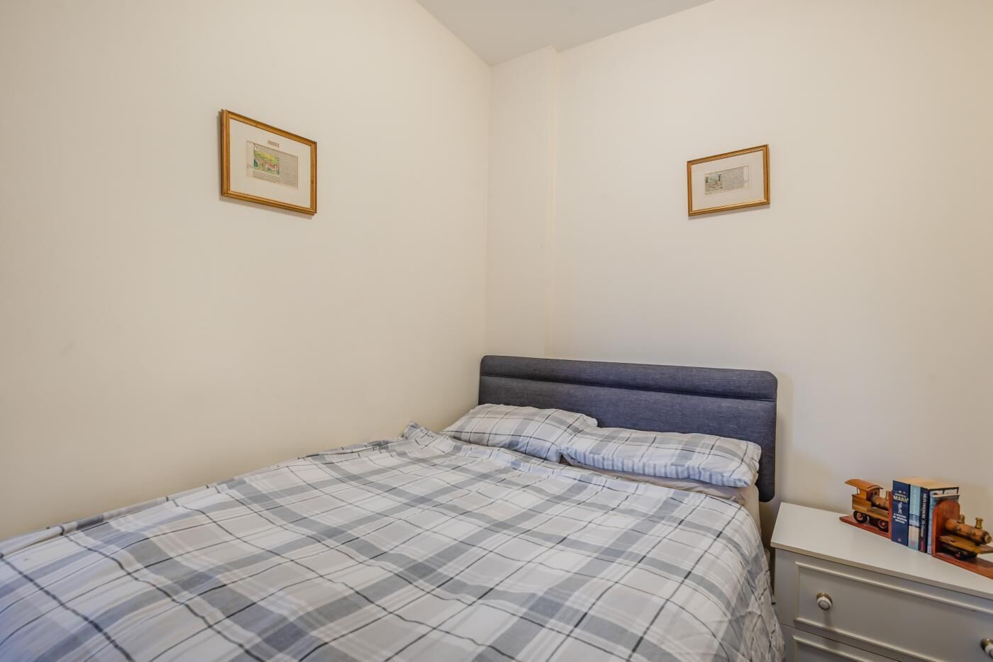 Une chambre à coucher avec un lit, une table de chevet et deux tableaux encadrés accrochés au mur.