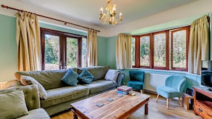 Ein gemütliches Wohnzimmer mit einer Couch, Sesseln, einem Holztisch und einem Fernseher.