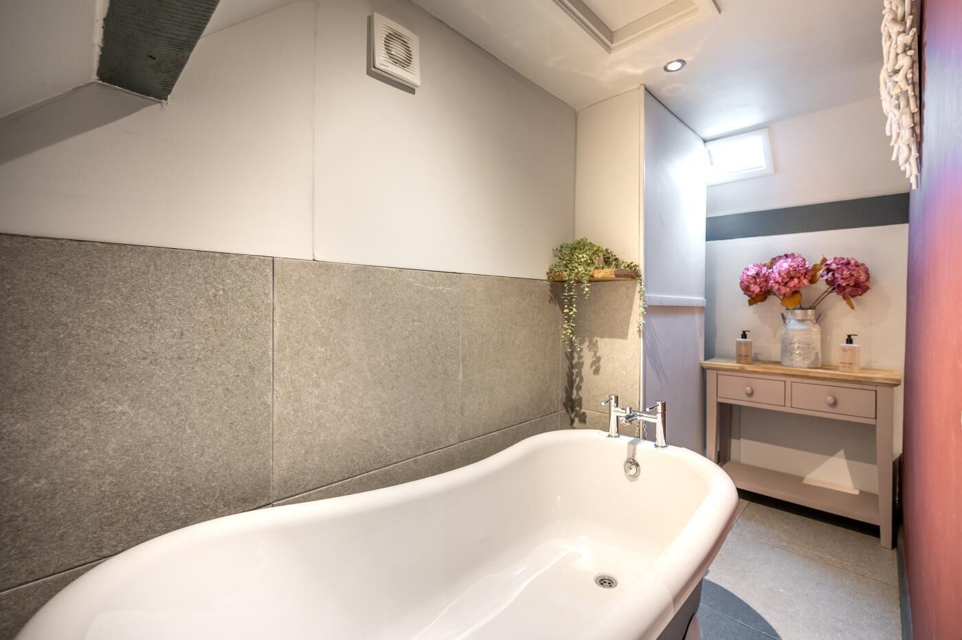 A modern bathroom with a freestanding bathtub, a small window, and a vanity with a mirror and two bottles.