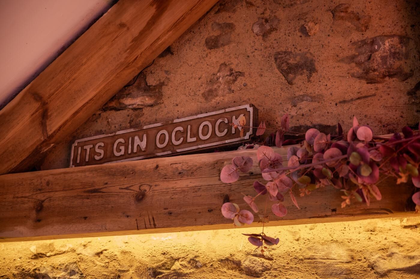 Uma placa de madeira com o texto 'ITS GIN OCLOCK' e um ramo com folhas rosa.