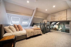 Ein Schlafzimmer mit Bett, Nachttisch, Fenster, einer Treppe und Blick auf einen Raum mit einer Katzenstatue.