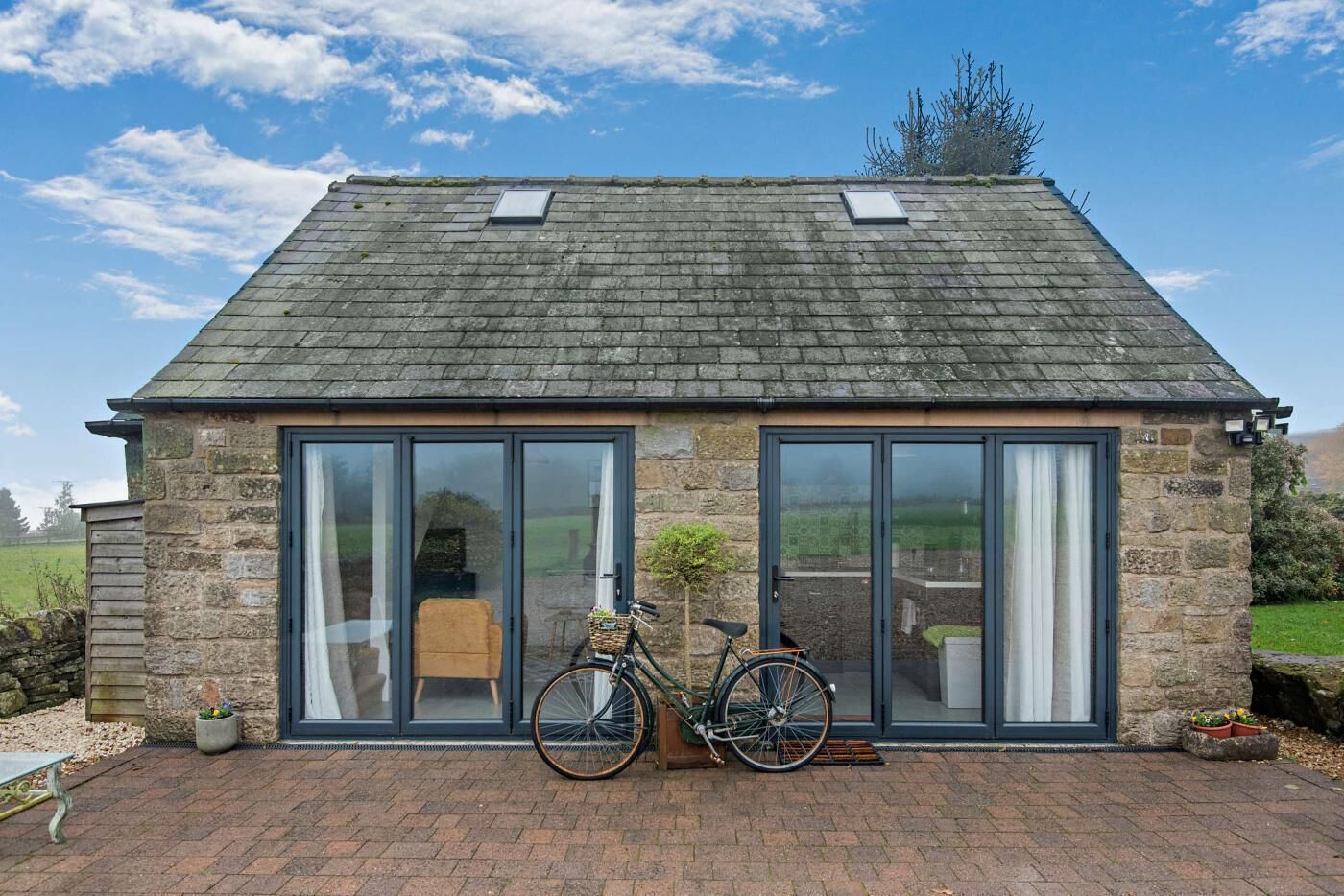 Un bâtiment en pierre avec un toit en pente, de grandes portes vitrées et un vélo garé à l’extérieur.