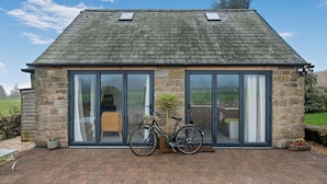 A stone building with a sloped roof, large glass doors, and a bicycle parked outside. - 3 Bed in Ashover (oc-w30175) (Ashover)