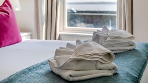 Un letto rifatto con una coperta blu e due asciugamani piegati su una panca azzurra.