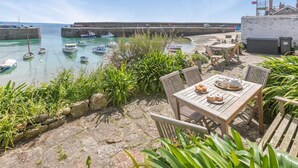 Un patio con vista sul mare, con un tavolo apparecchiato per la cena, che si affaccia su un porto con barche e un muro di pietra.