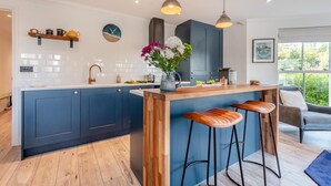 A modern kitchen with a central island, bar stools, pendant lighting, and a view of the outdoors.