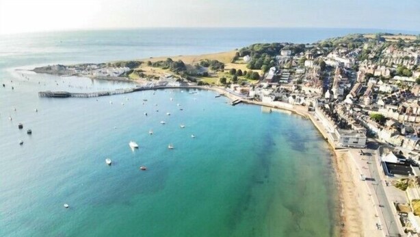 An aerial view of a coastal town with a marina, sandy beach, and residential buildings.