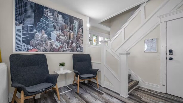 Een modern interieur met twee donkere stoelen, een stadsgezicht schilderij, een kleine tafel met een plant en een trap die naar een deur leidt.