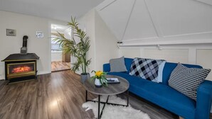 Een moderne woonkamer met een houtkachel, een blauwe bank en een potplant.