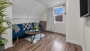 Een gezellige kamer met een blauwe bank, een ronde salontafel en een groot raam met gordijnen.