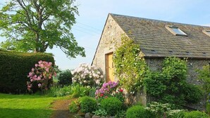 Een stenen huis met schuin dak, een duidelijke deur en een tuin met diverse planten en bloemen.