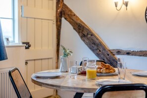 Ein Esstisch mit Croissants, Saft und einem Krug, in einem Zimmer mit sichtbarem, rustikalen Holzbalken und Blick ins Freie.