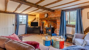 Ein gemütliches Wohnzimmer mit freiliegenden Holzbalken, einem Kamin aus Ziegelsteinen, einem Fernseher und bequemen Sitzmöglichkeiten.