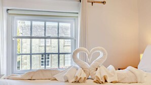 Une chambre d’h ôtel avec une grande fenêtre, un lit recouvert de draps blancs et deux serviettes en forme de cœur posées sur le lit.