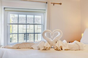 Une chambre d’hôtel avec une grande fenêtre, un lit recouvert de draps blancs et deux serviettes en forme de cœur posées sur le lit.