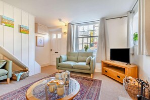 Un salon avec un canapé, un téléviseur, une table basse avec des tasses, un escalier et une fenêtre avec des rideaux.