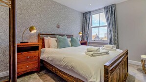 Een slaapkamer met een houten bed, twee nachtkastjes, een raam met gordijnen en uitzicht op gebouwen.