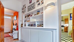 Een hal met witte inbouwplanken, een zwart-wit betegelde vloer en een deur naar een keuken.