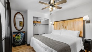 A bedroom with a large bed, a ceiling fan, a wooden headboard, a wardrobe, and a painting on the wall.