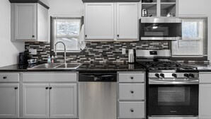 A modern kitchen with white cabinets, a black countertop, a dishwasher, a stove, and a microwave.