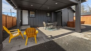 A covered patio area with a table and chairs, a wooden fence, and a door.