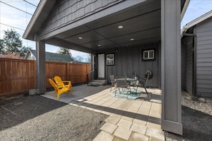 A covered patio with a table and chairs, a wooden fence, and a wooden deck.