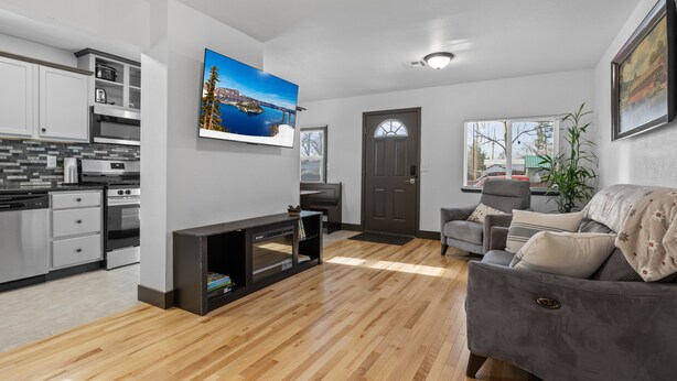A modern living room with a flat-screen TV, grey sofa, and a dining area with a kitchen in the background.