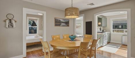 A dining area with a round wooden table, six chairs, a woven pendant light, and a floral rug.