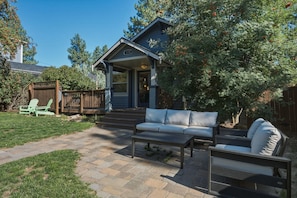 A residential property with a patio area featuring a sofa and a coffee table, a wooden deck, and a fenced yard.