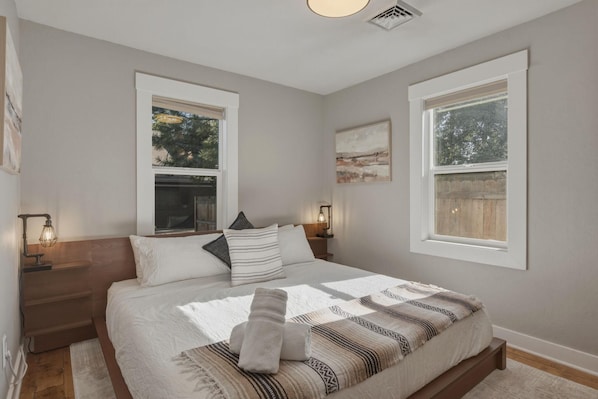 A bedroom with a large bed, two bedside tables with lamps, a window with a view of trees, and a painting on the wall.
