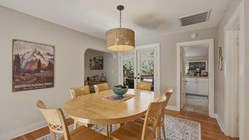 A dining area with a round wooden table, six chairs, a hanging woven light fixture, and a poster on the wall.
