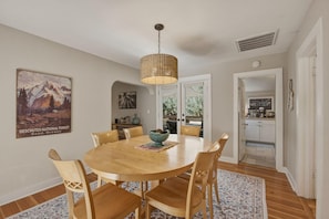 A dining area with a round wooden table, six chairs, a hanging woven light fixture, and a poster on the wall.
