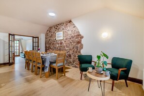 Un coin repas agrémenté d’un mur en pierre, d’une table à manger en bois, de chaises et d’une petite table ronde sur laquelle est posée une plante.