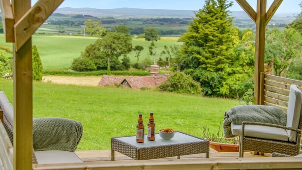 Une terrasse en bois, meublée de meubles en osier, qui offre une vue sur un paysage verdoyant.