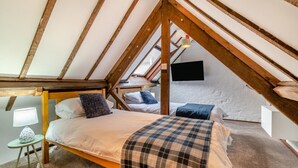 Une chambre avec un plafond en pente, des poutres en bois, un lit, une table de chevet avec une lampe et un téléviseur fixé au mur.