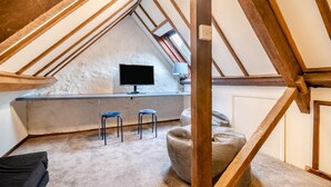 Une chambre aménagée dans les combles, avec un plafond en pente, une télévision, deux tabourets et une fenêtre.