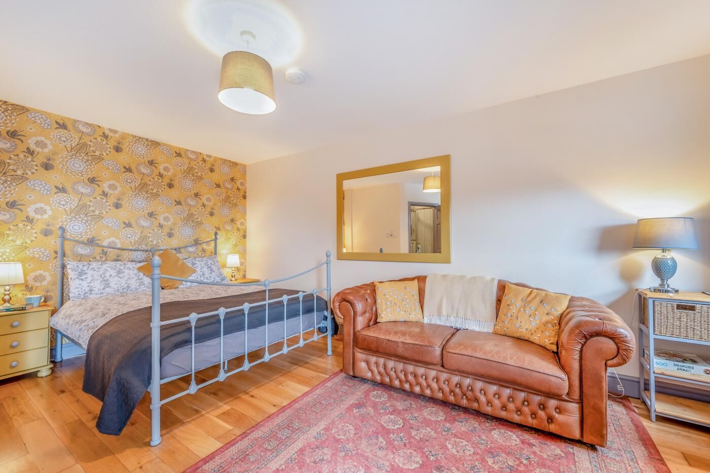Ein Schlafzimmer mit einem Bett, einem Ledersofa, einem Spiegel und einem Nachttisch mit einer Lampe.
