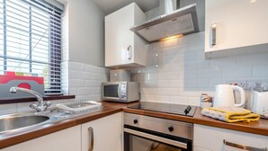 Una cocina moderna con armarios blancos, un lavamanos de acero inoxidable, un microondas, un horno y una tetera en la encimera.