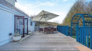 A wooden deck with outdoor furniture, a large umbrella, and a blue gate. - 3 Bed in St. Dogmaels (oc-y30253) (Saint Dogmaels)