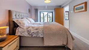 A bedroom with a bed, bedside table, lamp, and a view of the outdoors through a door. - 3 Bed in St. Dogmaels (oc-y30253) (Saint Dogmaels)